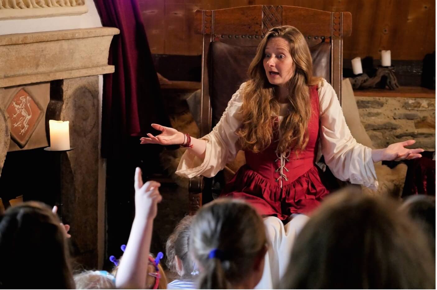 Eine Frau im historischen Gewand erzählt Kindern eine Geschichte am Kamin, die aufmerksam zuhören und Fragen stellen.